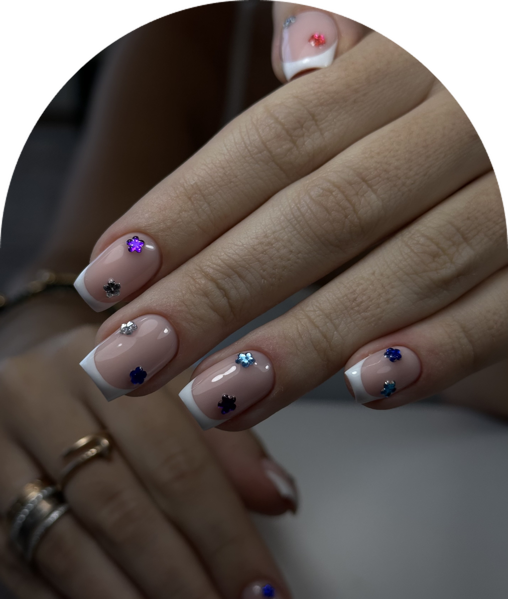 White French tip nails with colorful flower gems at Hera's Beauty Salon